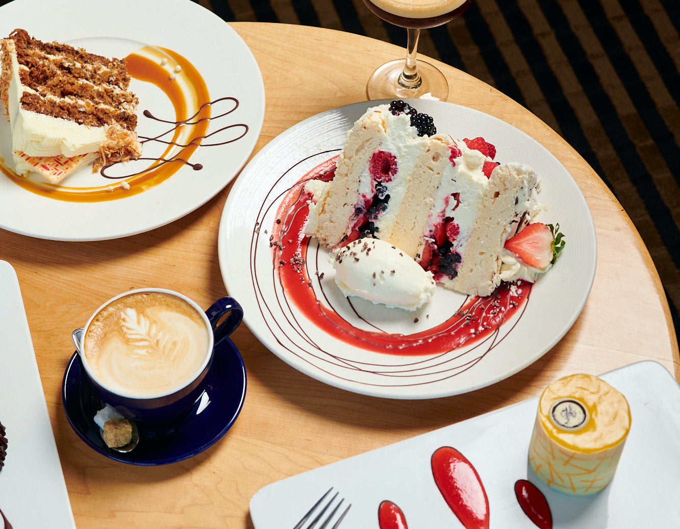 A slice of Carrot Cake, a slice of Boccone Dolce, a latte, and The Passion on a table at Papa Haydn